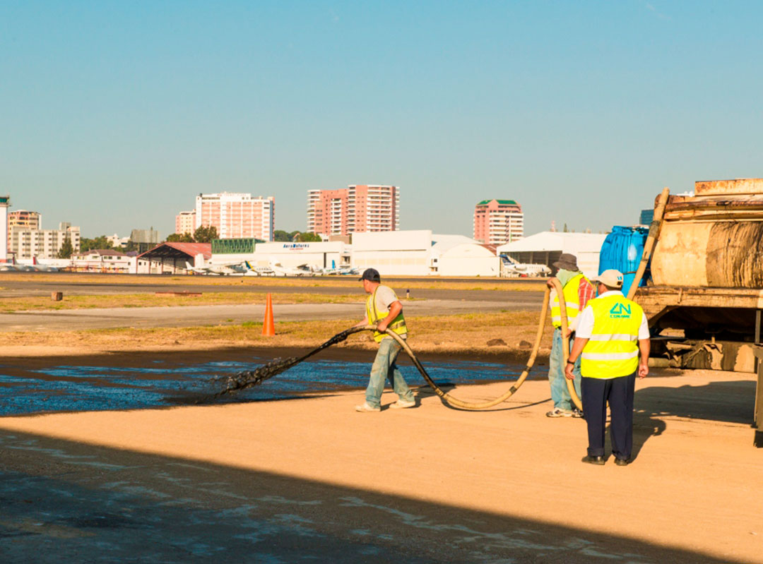 Workers using a hose from a water truck to apply a surface seal of HiPower Seal Black to an airport apron